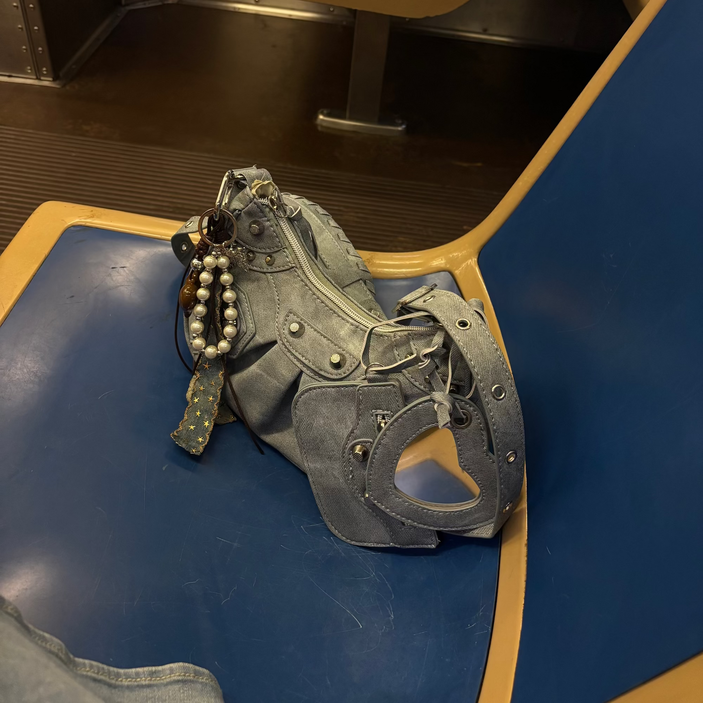 Blue leather handbag with a strap on a blue seat inside a train.