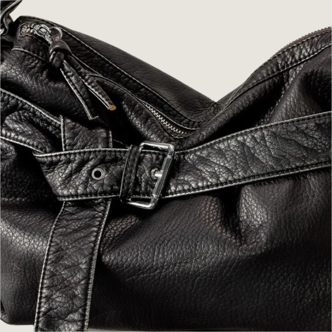 Close-up of a black leather bag with a strap and buckle on a light gray background